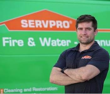 Stout young man with brown hair and slight beard and arms folded wearing a SERVPRO golf shirt by a SERVPRO truck