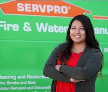 Young woman with long dark hair smiling with arms folded standing next to a SERVPRO truck
