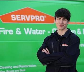 Tall young man with dark, tousled hair and a black SERVPRO zip sweater by a green SERVPRO truck