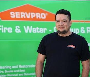 Man in late 30s with shorter dark hair and chin beard, wearing a SERVPRO T-shirt, standing next to a SERVPRO truck 
